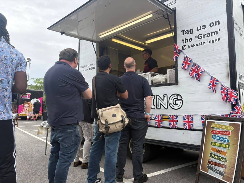 Freshly prepared meals served from KK Catering food truck in UK, with customers ordering at busy event.